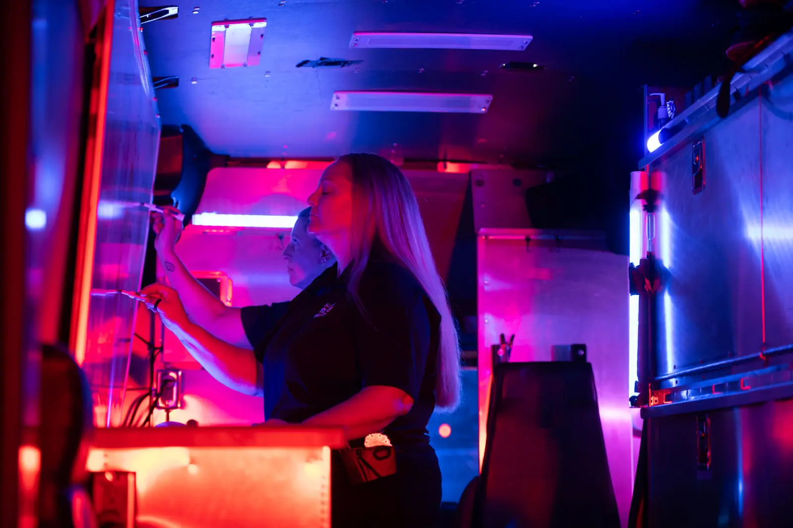 Two people work inside a dimly lit control room with blue and pink lights, writing on a whiteboard about the Bellevue Police Foundation.