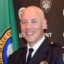 Assistant Chief Carl Kleinknecht stands in a police uniform before a police department backdrop and a state flag. Bellevue Police Foundation