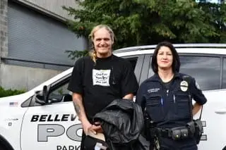 A person proudly holding a Foundation Award stands beside a police officer in front of a Bellevue Police vehicle.