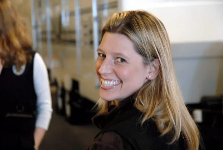 A person with long blonde hair smiles while looking back, clearly enjoying the Bellevue Police Foundation Service Awards. They are indoors, and another individual is partially visible in the background, also engaged in the event's lively atmosphere.