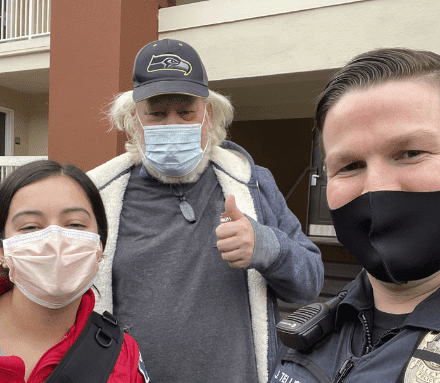 Three people wearing masks pose for a selfie, one giving a thumbs-up, representing community spirit that supports Bellevue Police Foundation Programs. A fourth person stands partially visible to the side, adding a touch of mystery to this moment captured in unity and support.