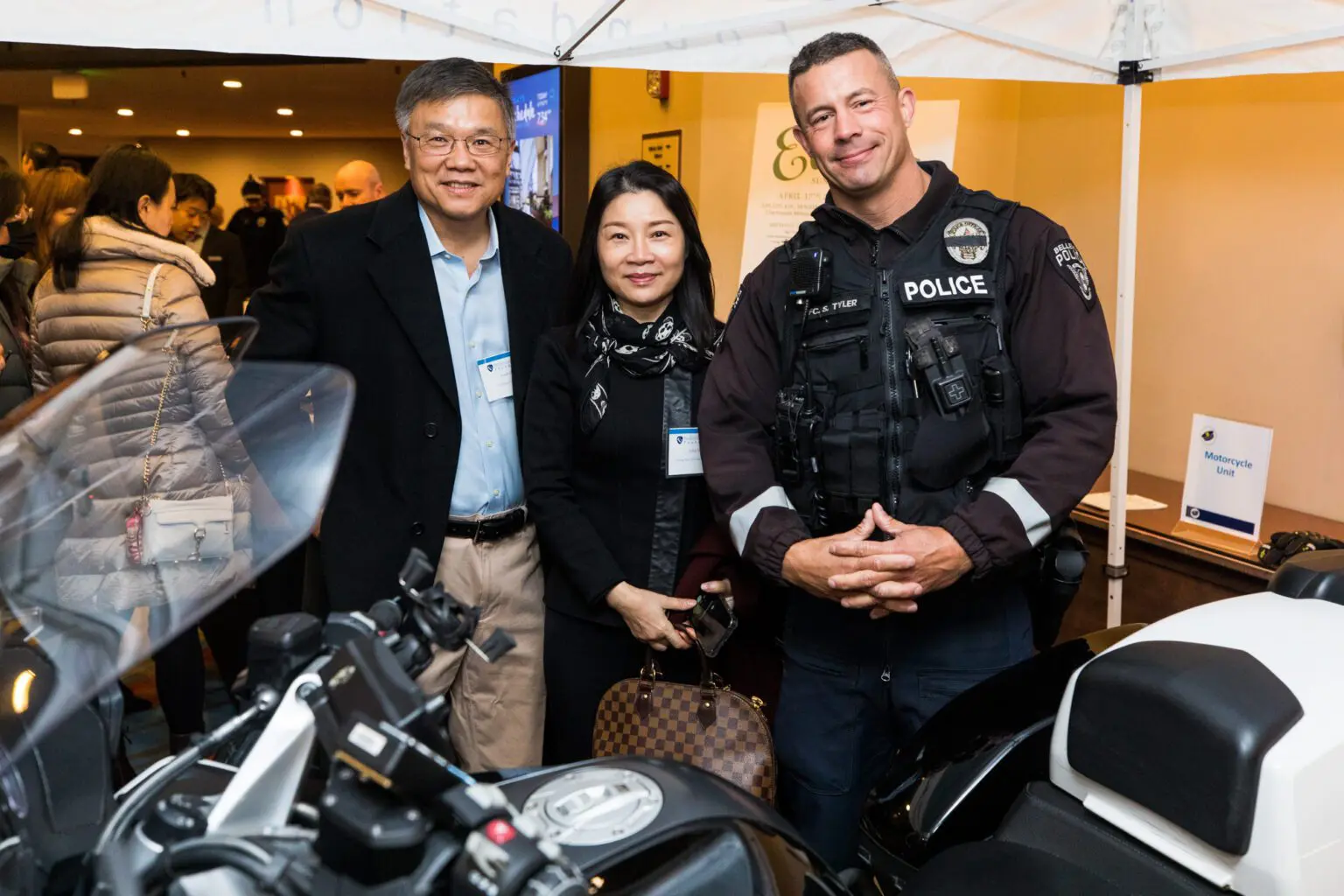 A police officer stands with two people posing next to a motorcycle at a 2022 Breakfast Fundraiser event.