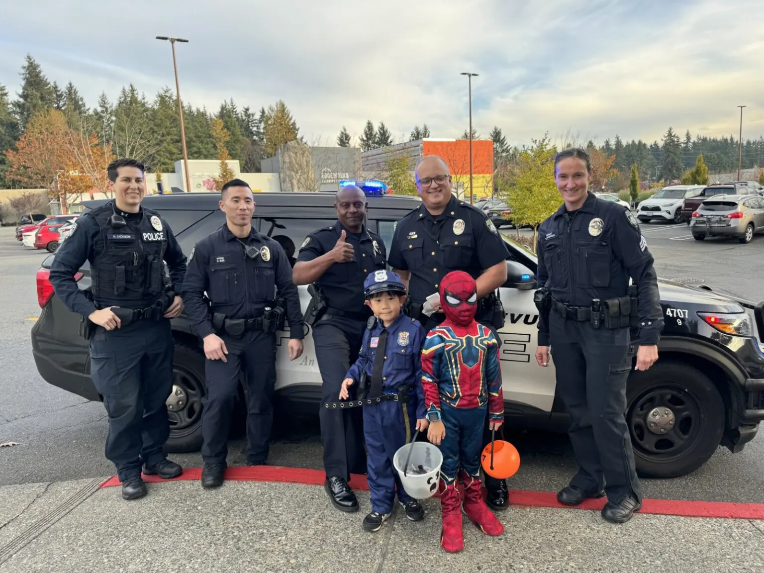 Bellevue Police officers pose with two children dressed as a police officer and Spider-Man in front of a police car, creating some Halloween fun in the parking lot.