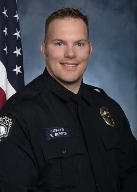 Officer Kevin Bereta, in full uniform, stands proudly before an American flag, embodying the spirit of duty and commitment.