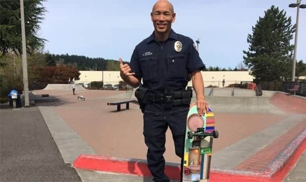 A police officer in uniform, recently honored with a Foundation Award for community outreach, holds a skateboard and smiles at a skate park. Bellevue Police Foundation
