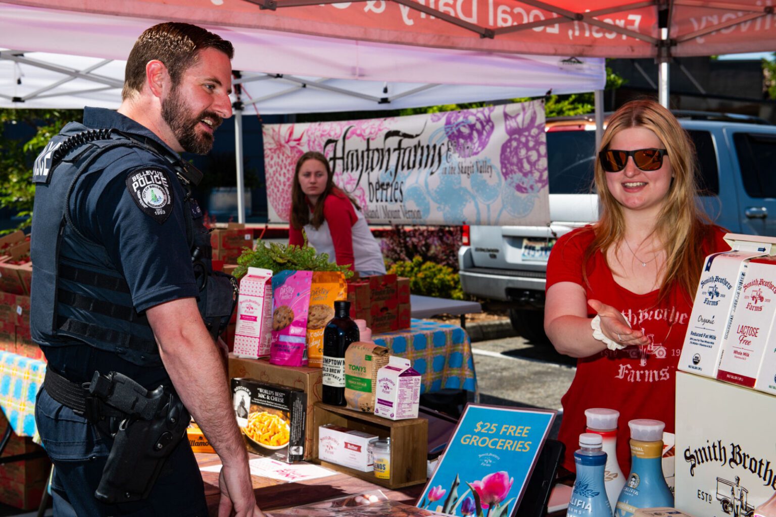 A Bellevue Police officer engages with a vendor at an outdoor market stall displaying various goods, offering foundation help through community interaction.