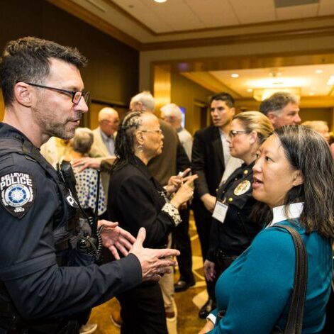 At the Bellevue Police Foundation Annual Breakfast, a police officer engages in conversation with a woman amid the bustling crowd.