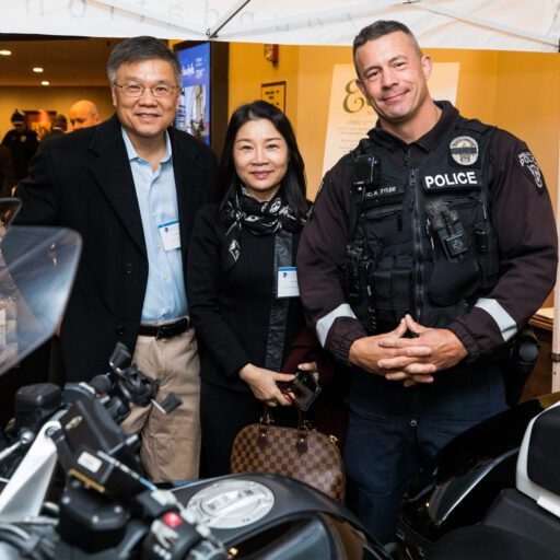 A police officer stands with two people posing next to a motorcycle at a 2022 Breakfast Fundraiser event.