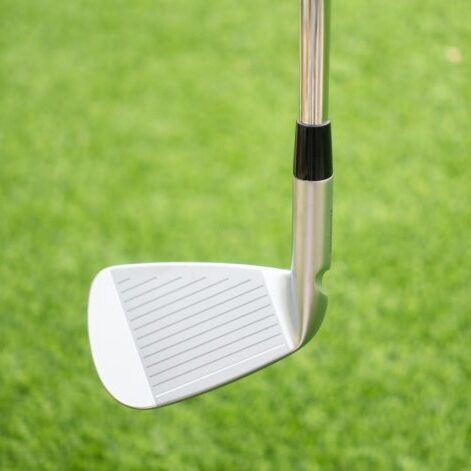 Close-up of a shiny silver golf iron head with striped grooves on a lush green lawn, ideal for sport themes.