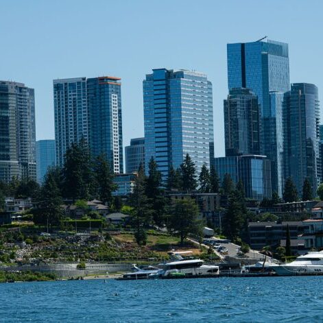 The city skyline, adorned with modern high-rise buildings near the waterfront, stands proudly alongside the vibrant support of Bellevue Police Foundation's corporate partners. Trees grace the shore, where boats are peacefully docked, creating a harmonious urban oasis.