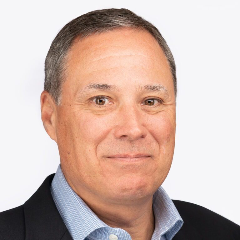 A man in a suit and blue shirt, likely a member of the Bellevue Police Foundation Board of Directors, looks at the camera with a neutral expression.