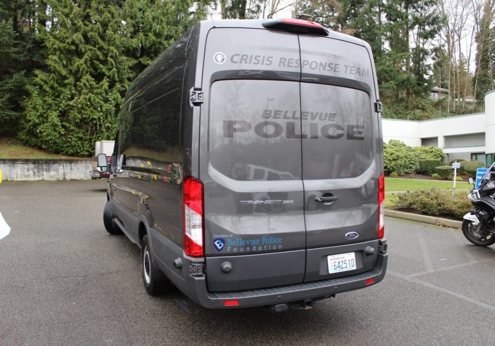 A gray van with "Crisis Response Team" and "Bellevue Police" markings is parked outdoors near trees and a building. Bellevue Police Foundation