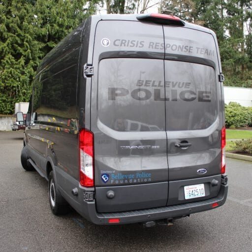 A gray van with "Crisis Response Team" and "Bellevue Police" markings is parked outdoors near trees and a building. Bellevue Police Foundation