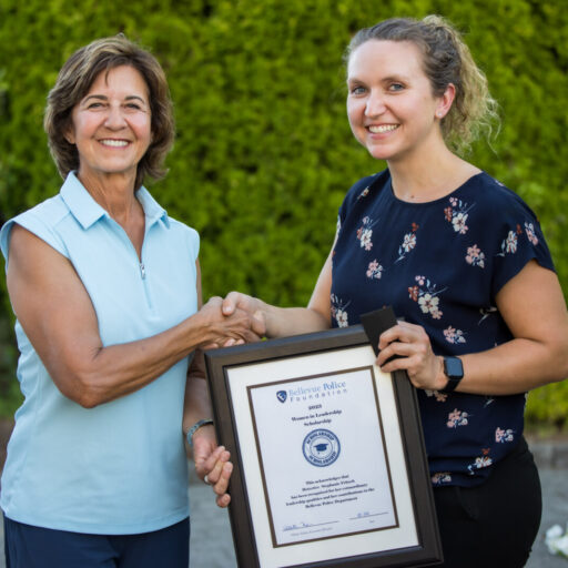 Two women smiling; one holds a framed certificate while they shake hands outside, with greenery in the background. Celebrating the success of the Women in Leadership 2023 Scholarship Program, these inspiring leaders reflect on their journey and growth.