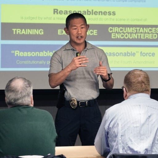 A man in a gray polo shirt conducts a presentation on reasonableness and use of force. Three people listen attentively in front of a projected slide. Bellevue Police Foundation