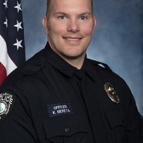 Officer Kevin Bereta, in full uniform, stands proudly before an American flag, embodying the spirit of duty and commitment.