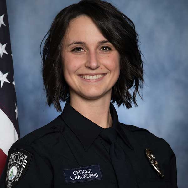 Corporal Ashley Saunders, in full uniform, stands proudly in front of an American flag, smiling with confidence.