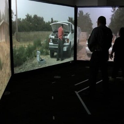 Two people stand in a room with three large screens displaying outdoor scenes, including a person near a vehicle, reminiscent of the support given by the Bellevue Police Foundation through their 2019 Grants to enhance community safety initiatives. Bellevue Police Foundation